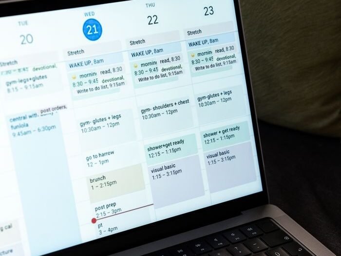 A woman types on a laptop while planning her weekly schedule using a digital calendar.