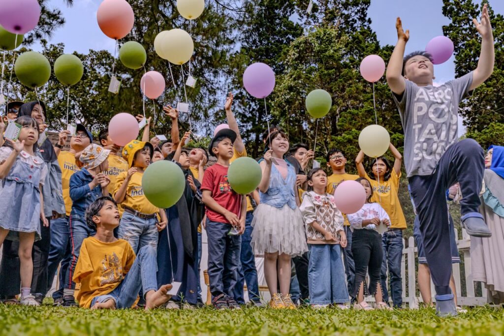 A joyful gathering of children releasing balloons in Bandung, Indonesia, during a festive celebration.