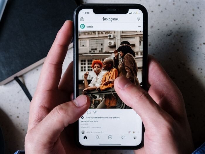 Close-up of hands holding a smartphone browsing Instagram with a notebook and pen nearby.