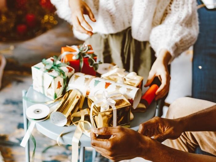Two people wrapping Christmas gifts at home, creating a cozy holiday atmosphere.
